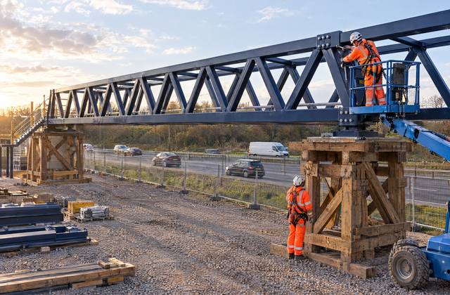 A site team assembling the blue steel truss on trestles at sunset